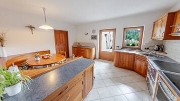 Cucina con zona pranzo, mobili in legno, forno a incasso e finestra con vista sul verde.