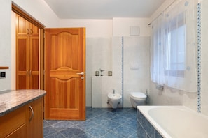 A bathroom with a wooden door, a bidet, a toilet, and a bathtub.