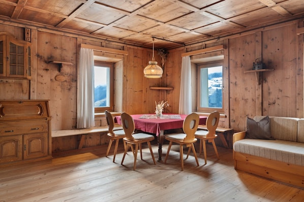 A wooden cabin interior with a dining table, chairs, a sofa, and a wooden cabinet.