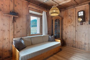 A wooden interior with a sofa, a hanging light fixture, a wooden cabinet, and a clock on the wall.