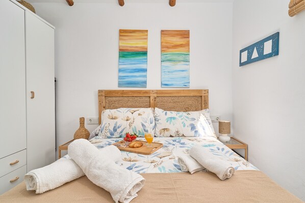 A neatly made bed with a floral pattern, a wooden headboard, and two wall-mounted paintings.