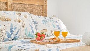 A bed with floral bedding, a tray with strawberries and croissants, and two glasses of orange juice.