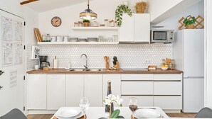 A modern kitchen with white cabinetry, a wooden countertop, a microwave, a refrigerator, and a dining area with a table set for two.