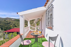 A balcony with a table set for breakfast, a chair, and a view of a hilly landscape.