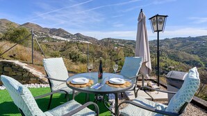 A table set outdoors with chairs, a bottle, and glasses, overlooking a mountainous landscape.