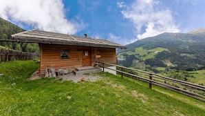 Een houten chalet met een schuin dak, een houten veranda en uitzicht op een bergachtig landschap.