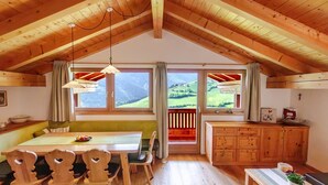 Een houten interieur met een eettafel, stoelen, een bank, een keukenhoek en grote ramen met uitzicht op de omgeving.