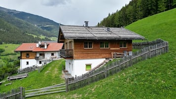 Une maison en bois dotée d’un balcon, entourée d’une clôture en bois et d’une colline verdoyante.