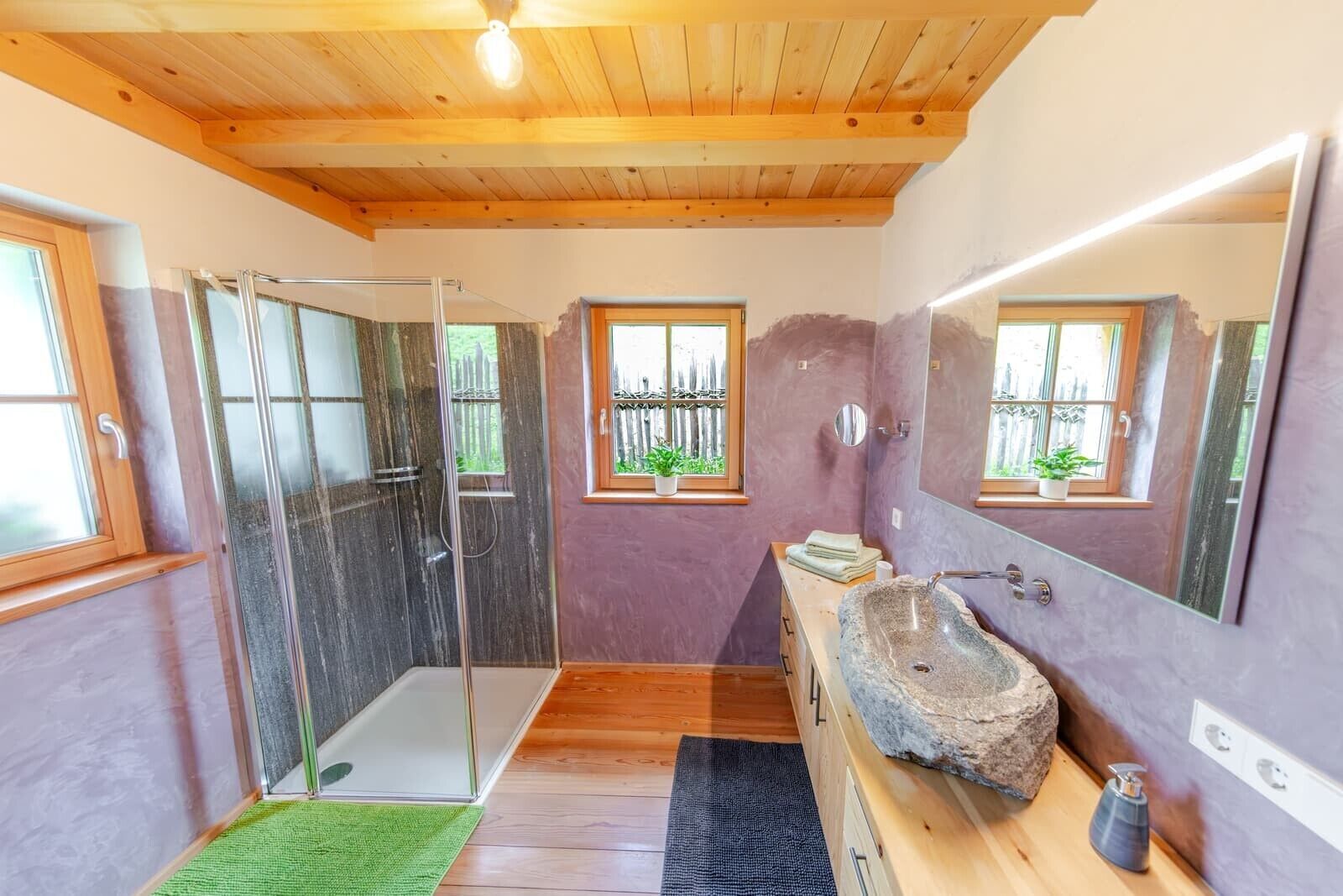 Een badkamer met een douchecabine van glas, een stenen wastafel, houten vloeren en een grote spiegel.