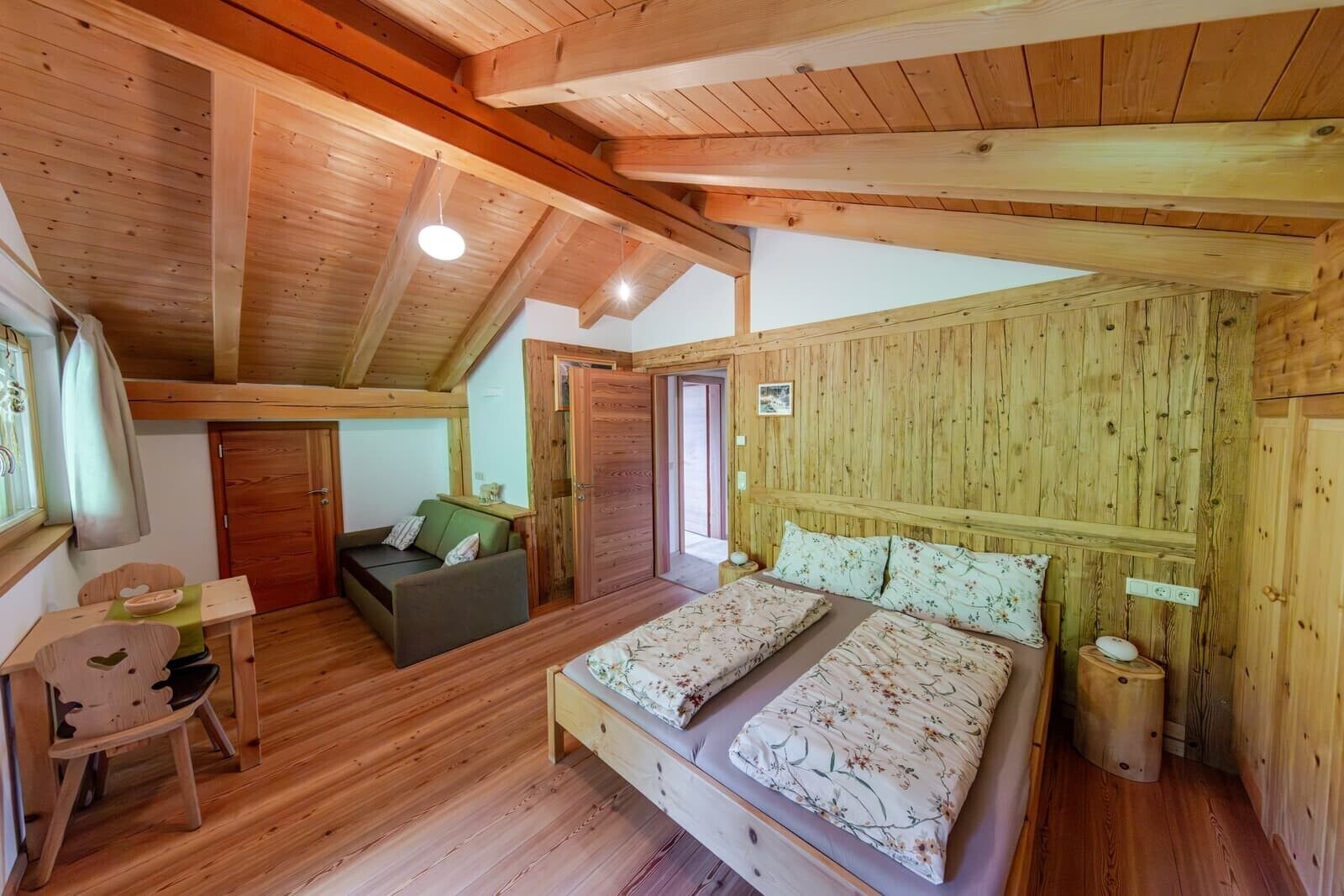 Una cabaña de madera con un dormitorio en la buhardilla, una pequeña zona de estar y techo de madera.
