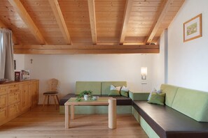 Una stanza con travi in legno, un divano verde, un tavolo di legno e una sedia.