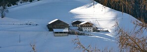 Un paysage enneigé avec deux bâtiments en bois, l’un doté d’un toit en pente et l’autre d’un toit plat, le tout entouré de neige et d’arbres.