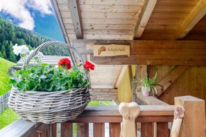 Un balcon en bois orné d’un panier en osier rempli de fleurs, d’une enseigne en bois et d’un banc en forme de cœur.
