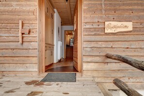 Interior de una cabaña de madera con una puerta de madera, un letrero que dice 'Almhütte' y una zona de cocina visible.