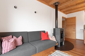 Ett modernt vardagsrum med en grå soffa, röd- och vitrutiga kuddar, en svart vedkamin och ett träpanelat tak.
