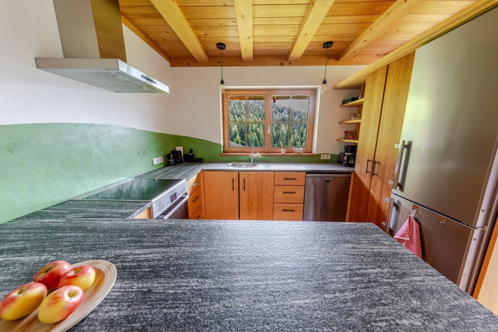 Una cucina con mobili in legno, frigorifero in acciaio inossidabile, una finestra vista alberi e un piano di lavoro in granito.