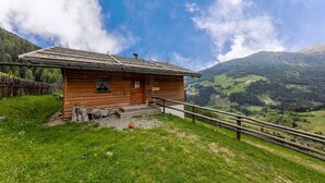 Eine Holzhütte mit geneigtem Dach, einer Holzterrasse und Blick auf eine Berglandschaft.
