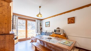 Une pièce chaleureuse avec un banc en bois, une table sur laquelle est posée une carte, un téléviseur et une fenêtre avec des rideaux.