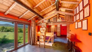 Ein geräumiger Raum mit Holzbalkendecke, großen Fenstern, einer Treppe und einem Bücherregal.