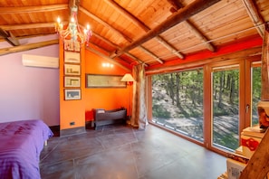 Ein Zimmer mit einem Bett, einer Bank, einer Kristallleuchter und großen Fenstern mit Blick auf einen Wald.