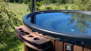 Ein Whirlpool mit Holzverkleidung, einem Metallschornstein und einem schönen Blick auf einen bewaldeten Hang.