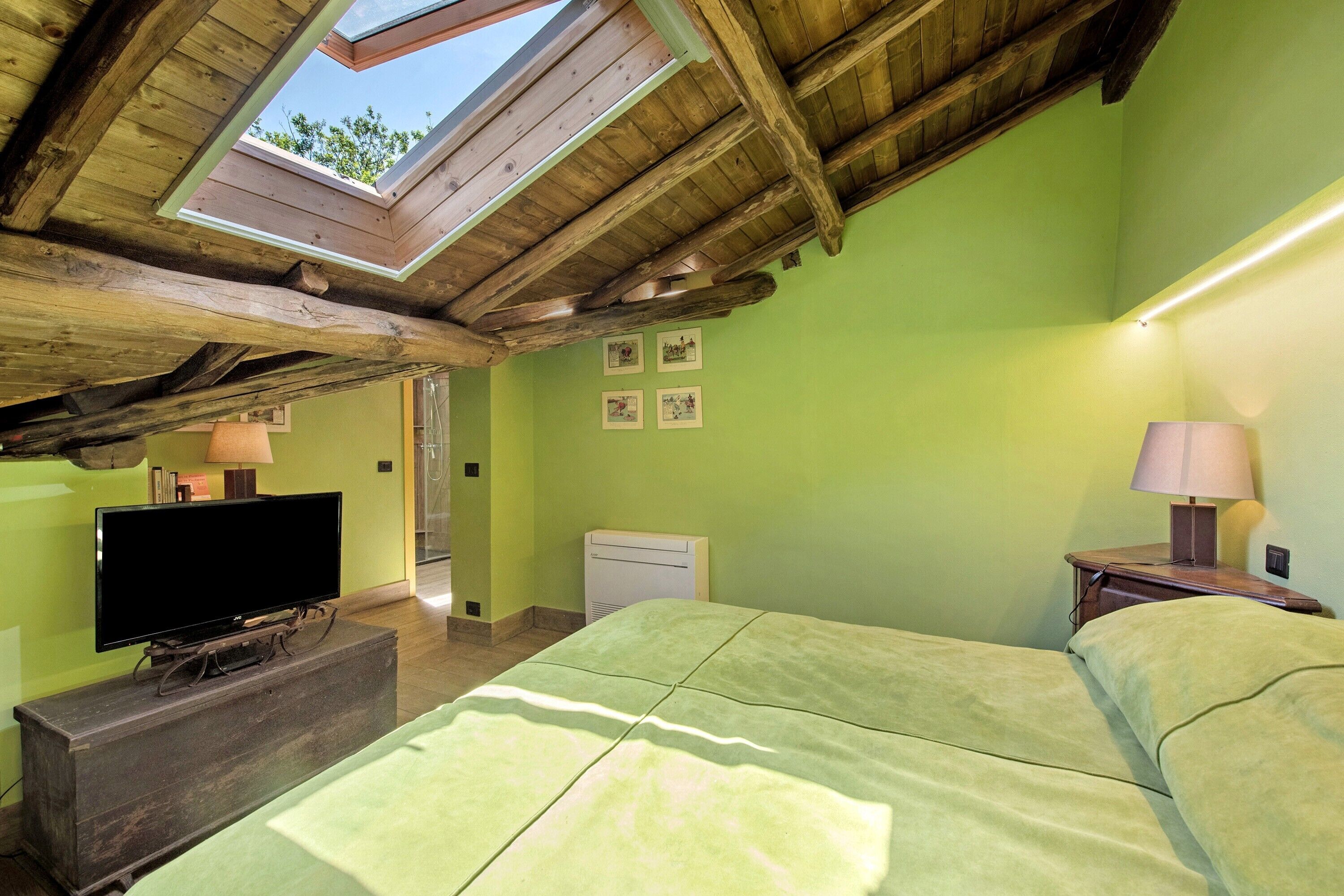 A room with a sloped ceiling, a bed, a television on a wooden dresser, and a small table with a lamp.