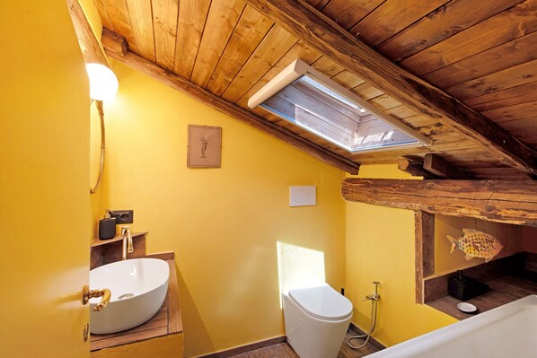 Ein Badezimmer mit Dachfenster, Holzboden und einem weißen Waschbecken.