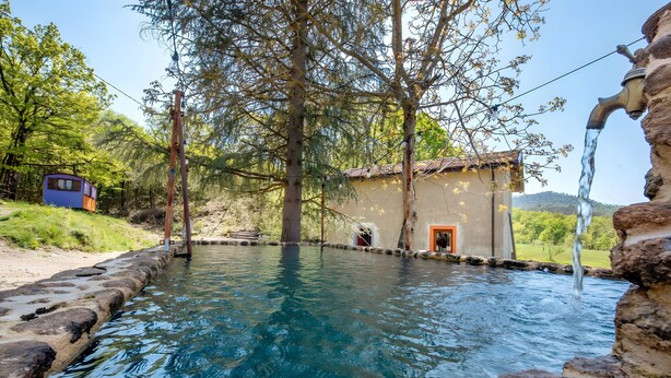 Ein klares Schwimmbecken mit Steinrand, einer Holzkonstruktion und einem Gebäude mit roter Tür.
