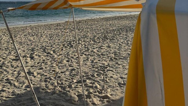A beach with a striped umbrella and a beach chair.