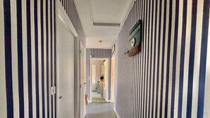 A hallway with striped walls and a carpeted floor, leading to a room with a bed and a nightstand.