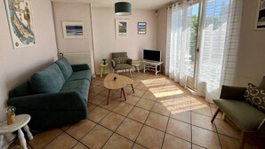 A living room with a sofa, a small table, a TV, and a window with curtains.