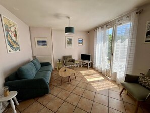 A living room with a sofa, a small table, a TV, and a window with curtains. - Location CARNAC - House 4 rooms - 6 people - Wifi (CARNAC)