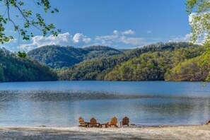 A lakeside view with a row of Adirondack chairs on the shore.