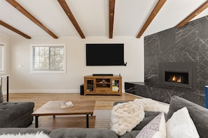 A living room with a fireplace, a flat-screen TV, wooden beams, and a sofa.