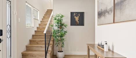 A wooden staircase leading to a landing with a potted plant and a framed deer head.