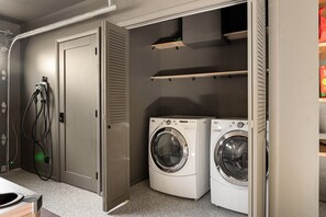 A laundry room with two washing machines, a door, and a wall-mounted shelf.