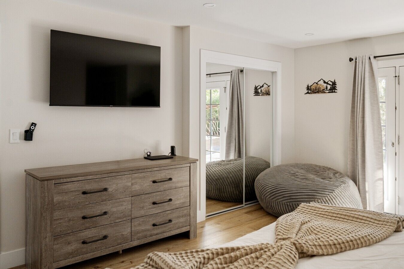 Un dormitorio moderno con un aparador de madera, un televisor de pantalla plana, un espejo y una cama con una colcha texturizada.
