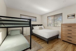 A room with bunk beds, a single bed, a dresser, and two windows with blinds.