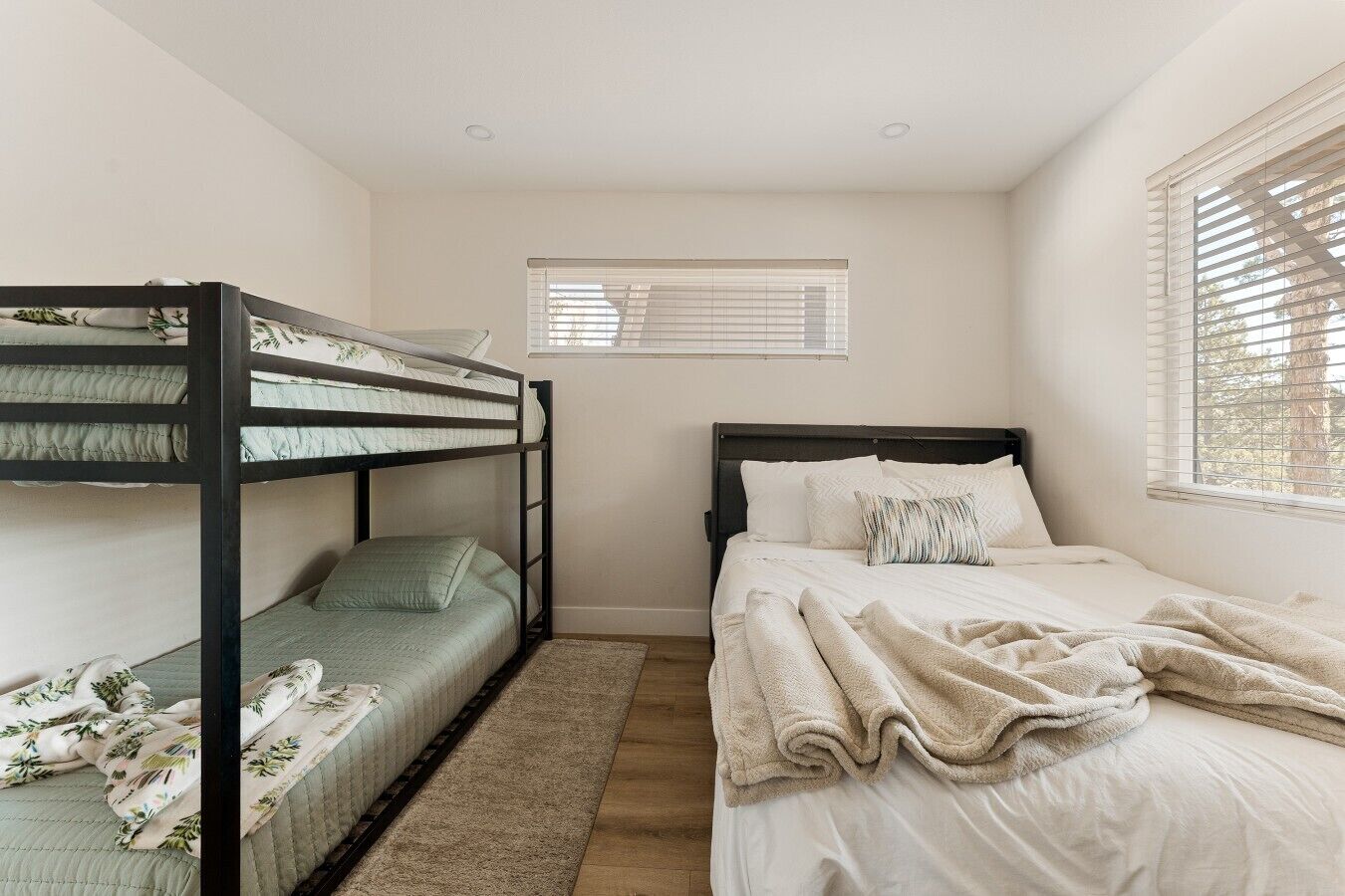 A bedroom with bunk beds, a single bed, a window with blinds, and a small rug.