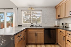 A modern kitchen with wooden cabinets, a stainless steel dishwasher, and a large window with blinds.