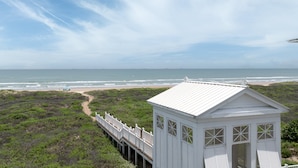 Una casa de playa blanca con terraza de madera que da al océano.
