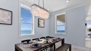 Un comedor con una larga mesa dispuesta para seis personas, ventanas amplias y vista al mar.