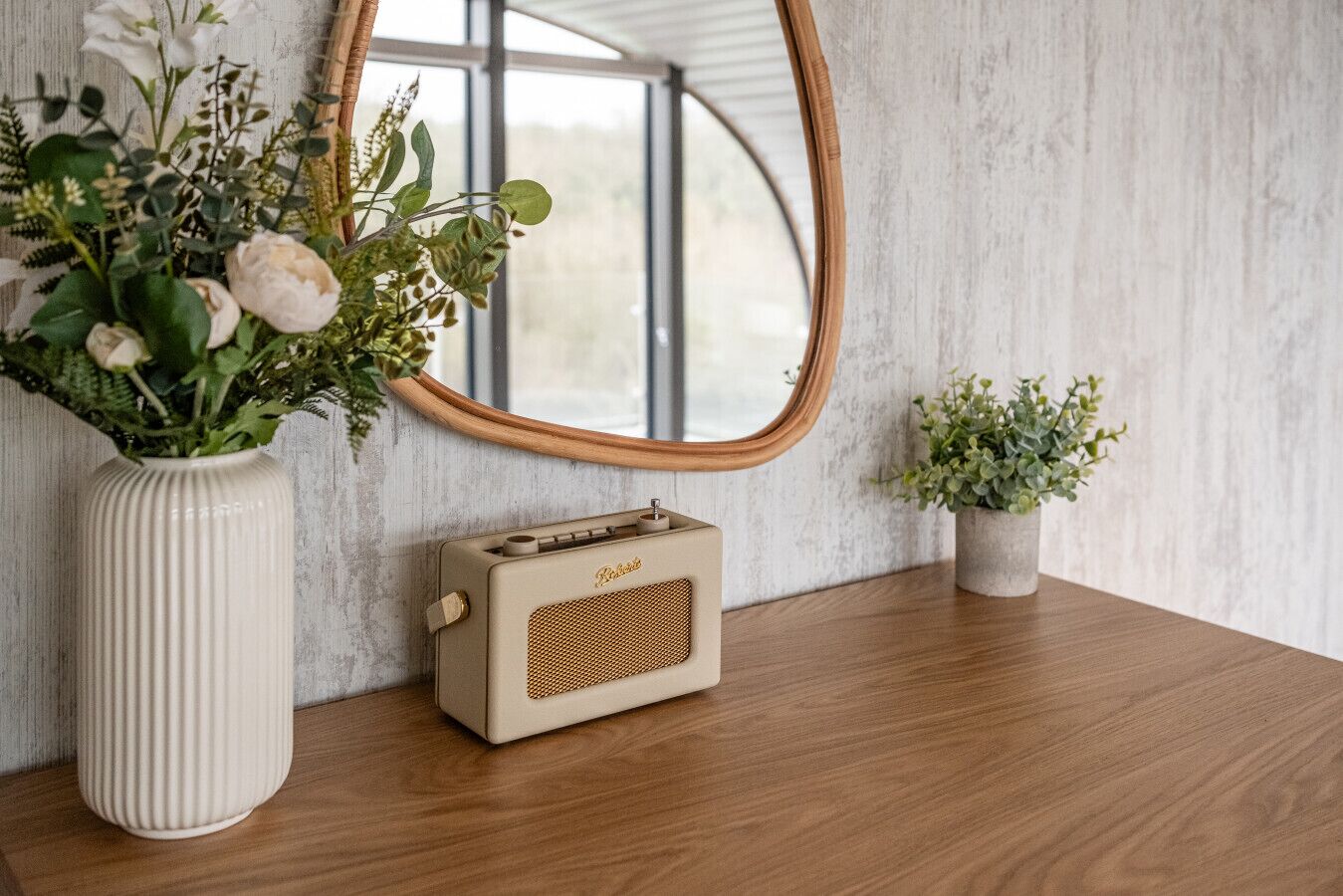 A vintage radio on a wooden table, a large mirror, and two potted plants.
