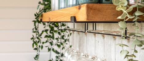 Una zona de cocina con un estante de madera con frascos y una barra colgante para copas de vino.