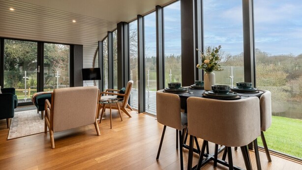 A modern dining area with a large table set for four, surrounded by large windows offering a view of the outdoors. - Fabulous Two Bedroom Eco Pod, Old Chalford Estate (Chipping Norton)
