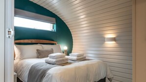 A cozy bedroom with a curved ceiling, a bed with neatly folded towels, and a bedside lamp. - Fabulous Two Bedroom Eco Pod, Old Chalford Estate (Chipping Norton)