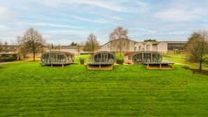 Three modern glass structures on a grassy field with a building in the background. - Fabulous Two Bedroom Eco Pod, Old Chalford Estate (Chipping Norton)