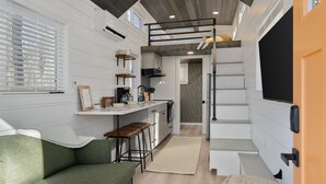 A compact kitchen with a dining area, a loft bedroom, and a staircase leading to a lofted sleeping area. - Tiny Home · Hot Tub · Fire Pit · Romantic Escape (Laurelville)