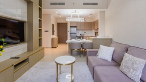 Una sala de estar moderna con un televisor de pantalla plana, un sofá, una mesa de centro redonda y un comedor con candelabro.