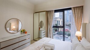 Una habitación de hotel con una cama grande, un espejo redondo, un aparador y vistas de la ciudad a través de la ventana.